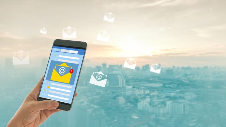 Elinde telefon tutan kişi, ekranda e-posta bildirimi ve havada uçuşan e-postalar