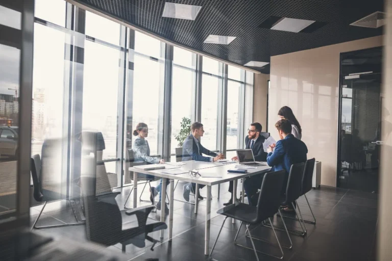 Modern ofis ortamında bir toplantı masasında oturan beş iş insanı
