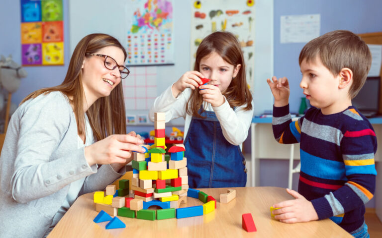 Öğretmen ve iki çocuk ahşap bloklarla kule inşa ediyor
